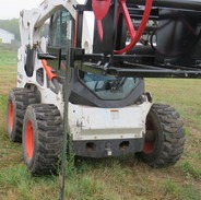 Image of a skid steer loader in grass field with a skid steer attachments above on it